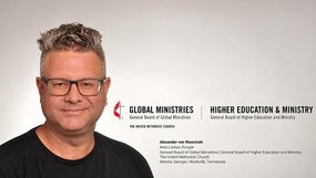 Links ein Mann mittleren Alters mit gegelten Haaren und Ohrring links sieht durch eine Brille freundlich direkt in die Kamera. Rechts das Logo der E m K und die Namen zweier Generalbehörden. Darunter der Name des Mannes und seine neue Stellenbezeichnung.