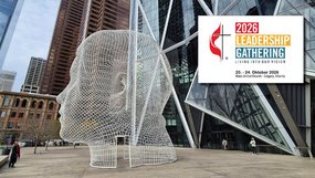 Auf einem Platz vor Hochhäusern steht ein großer menschlicher Kopf, der aus kleinen Drahtvierecken gebildet ist. Das Veranstaltungslogo besteht aus Kreuz und Flamme sowie englischem Text: »2026 Leadership Gathering. Living Our Vision«, Datum und Ort.