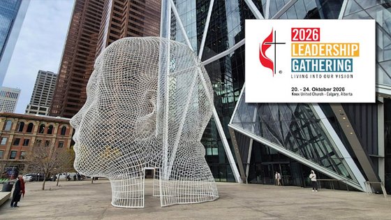Auf einem Platz vor Hochhäusern steht ein großer menschlicher Kopf, der aus kleinen Drahtvierecken gebildet ist. Das Veranstaltungslogo besteht aus Kreuz und Flamme sowie englischem Text: »2026 Leadership Gathering. Living Our Vision«, Datum und Ort.