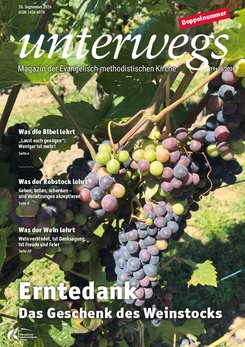 unterwegs Doppelausgabe 19-20/2026 Im Vordergrund hängen mehrere Trauben mit reifen und unreifen Beeren an einem Weinstock. Die Trauben zeigen unterschiedliche Farbtöne von Grün bis Dunkelviolett. Im Hintergrund sind grüne Blätter und weitere Weinreben zu sehen. Oben steht der Schriftzug 'unterwegs', darunter folgen weitere Textfelder mit Themen und Seitenzahlen. Unten befindet sich ein gelber Textfeld mit der Überschrift 'Erntedank Das Geschenk des Weinstocks'.