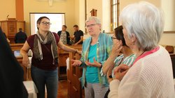 Fünf Menschen stehen in der Erlöserkirche Plauen der EmK und diskutieren. Eine Frau äußert sich gerade und macht mit ihren Armen und Händen eine betonende Geste. Drei andere Frauen blicken sie konzentriert an. Eine weitere Person ist nur teilweise sichtbar.