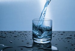 Ein Glas, das mit Wasser gefüllt wird als Sinnbild für den Durst des Menschen.