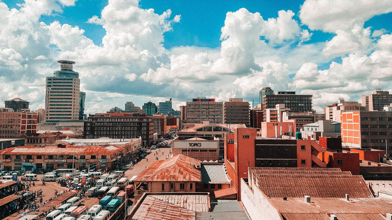 Stadtpanorama mit mehreren mehrst&ouml;ckigen Geb&auml;uden und belebten Stra&szlig;en unter bew&ouml;lktem Himmel.
